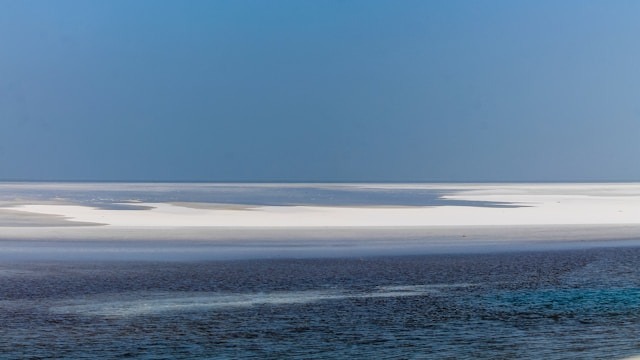 A vast white salt flat, the Rann of Kutch, under a clear blue sky.