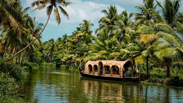 A traditional Kerala houseboat floating down a narrow backwater canal lined with palm trees.