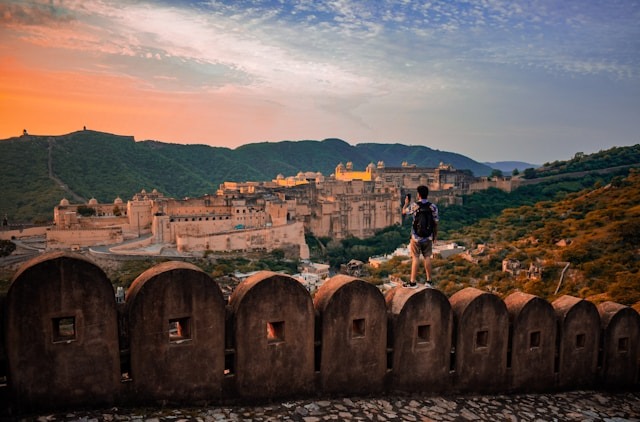 A man stands on a fort wall looking at Amer Fort in Rajasthan during sunset.