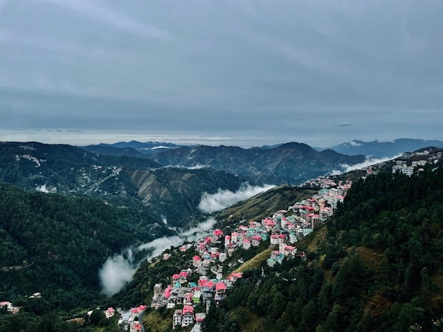A hillside city in Shimla, with colorful houses, green valleys, and clouds.