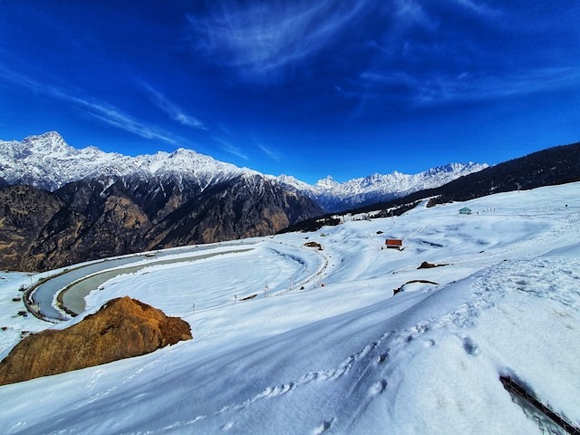 A snowy landscape in Auli, with a frozen lake and mountains under a deep blue sky.