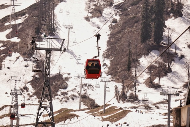 A red Gulmarg gondola car traveling up a snowy mountain.